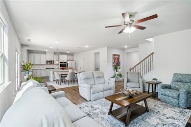 Living room featuring recessed lighting, light wood-type flooring, ceiling fan, and stairway