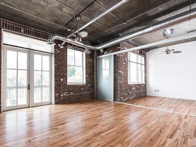 Unfurnished living room featuring brick wall, wood finished floors, and ceiling fan