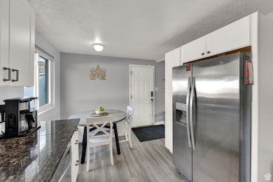 Kitchen with appliances with stainless steel finishes, a textured ceiling, light wood finished floors, white cabinets, and dark stone counters