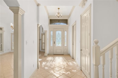 Foyer with a chandelier, a high ceiling, ornamental molding, light tile patterned floors, and decorative columns