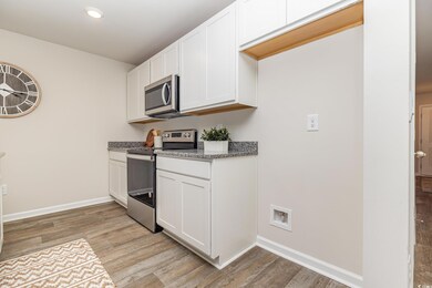 Kitchen featuring stainless steel appliances, white cabinets, light wood-type flooring, dark stone countertops, and recessed lighting