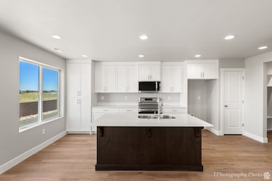 Kitchen featuring white cabinets, a center island with sink, stainless steel appliances, light wood finished floors, and recessed lighting