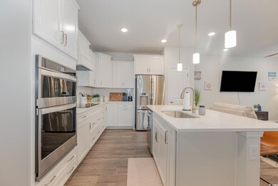Kitchen with stainless steel appliances, open floor plan, light countertops, light wood-style floors, and white cabinetry
