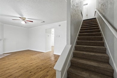 Stairs with a ceiling fan, ornamental molding, wood finished floors, and a textured ceiling