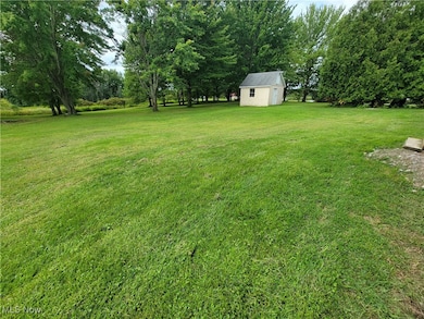 View of grassy yard featuring an outdoor structure and view of scattered trees