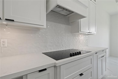 Kitchen with premium range hood, black electric stovetop, white cabinets, and marble look tiles
