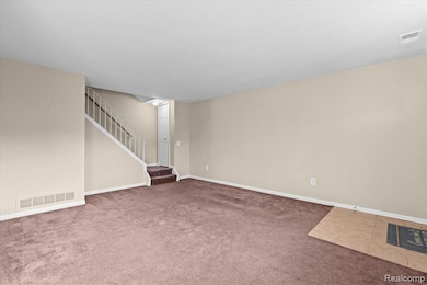 Unfurnished living room with light colored carpet, stairs, and light tile patterned flooring
