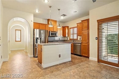 Kitchen with arched walkways, decorative light fixtures, stainless steel appliances, a kitchen island, and light stone counters