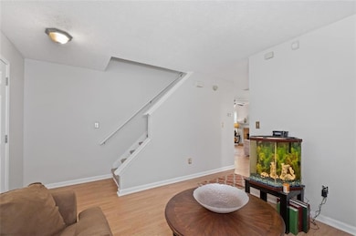 Living area with stairs, a textured ceiling, light wood finished floors, and baseboards