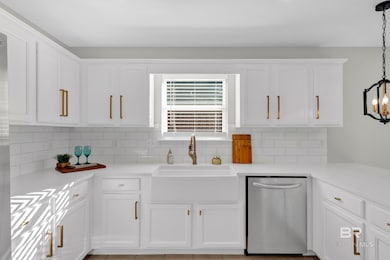 Kitchen with white cabinets, stainless steel dishwasher, pendant lighting, backsplash, and light stone countertops