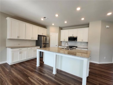 Kitchen with appliances with stainless steel finishes, a sink, dark wood-style floors, backsplash, and white cabinets