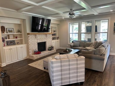 Living room with dark wood finished floors, a ceiling fan, a brick fireplace, coffered ceiling, and beam ceiling