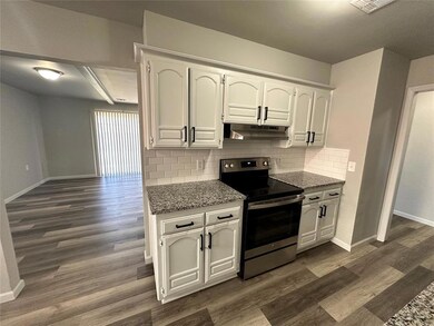Kitchen with stainless steel range with electric stovetop, under cabinet range hood, baseboards, tasteful backsplash, and dark wood-style flooring
