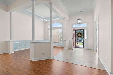 Entryway featuring crown molding, LVF, a chandelier, a high ceiling, and ornate columns