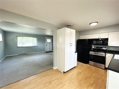 Kitchen with dark countertops, white cabinets, black appliances, light wood-type flooring, and open floor plan