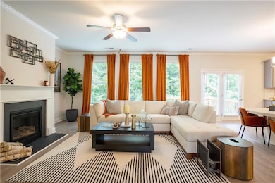 Living area with wood finished floors, ceiling fan, a glass covered fireplace, and crown molding
