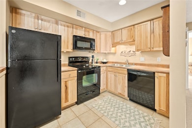 Kitchen with light brown cabinetry, black appliances, light countertops, light tile patterned floors, and recessed lighting