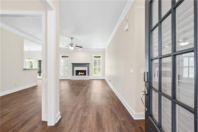 Unfurnished living room featuring ornamental molding, dark wood-style floors, ceiling fan, and a lit fireplace