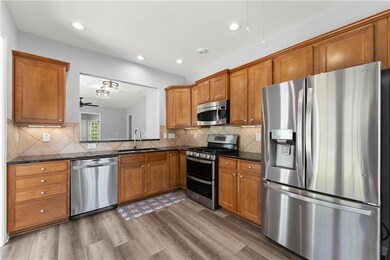 Kitchen with appliances with stainless steel finishes, brown cabinetry, backsplash, ceiling fan, and dark wood-type flooring