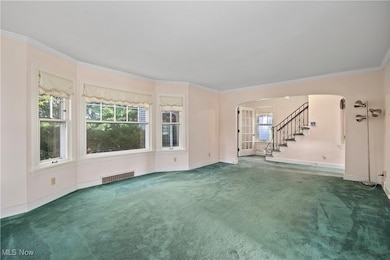 Unfurnished living room with arched walkways, stairway, ornamental molding, and carpet