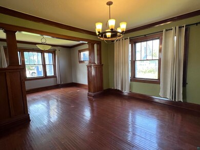 Empty room featuring a notable chandelier, ornate columns, dark hardwood / wood-style flooring, and a wealth of natural light