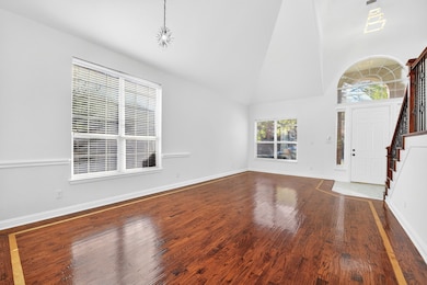 Unfurnished living room with stairway, high vaulted ceiling, and dark wood-type flooring