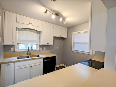 Kitchen featuring white cabinets, black dishwasher, light countertops, and healthy amount of natural light
