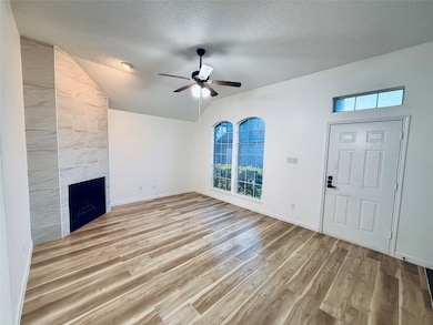 Unfurnished living room featuring a textured ceiling, lofted ceiling, light wood-style floors, a fireplace, and a ceiling fan