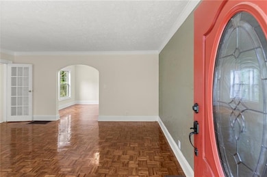 Entryway with arched walkways, baseboards, a textured ceiling, and crown molding