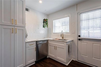 Kitchen with stainless steel dishwasher, a sink, dark wood-type flooring, and light stone countertops