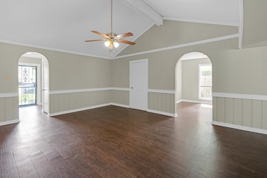 Unfurnished room featuring arched walkways, dark wood finished floors, beam ceiling, a wainscoted wall, and a ceiling fan