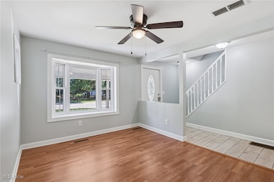 Unfurnished living room featuring light wood-style flooring, ceiling fan, and stairway