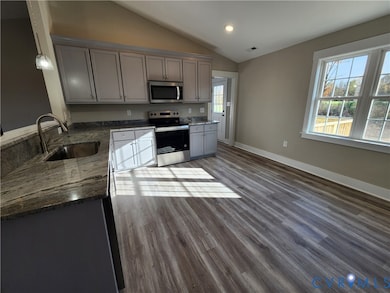 Kitchen with gray cabinets, dark stone countertops, appliances with stainless steel finishes, dark wood-style floors, and plenty of natural light