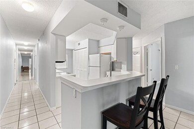 Kitchen with light tile patterned flooring, a textured ceiling, a kitchen breakfast bar, light countertops, and freestanding refrigerator
