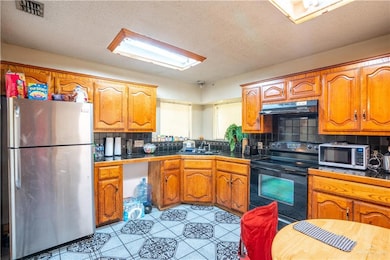Kitchen with appliances with stainless steel finishes, backsplash, brown cabinets, a textured ceiling, and under cabinet range hood