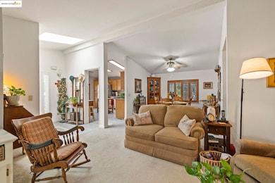 Living room with light colored carpet, lofted ceiling, ceiling fan, and a skylight