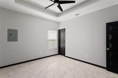 Empty room with electric panel, a raised ceiling, light marble finish floors, and ceiling fan