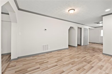 Unfurnished room featuring crown molding, light wood-style flooring, arched walkways, a textured ceiling, and baseboards