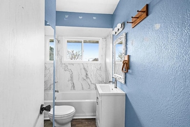 Bathroom with a textured wall, a bathtub, vanity, and dark wood-type flooring