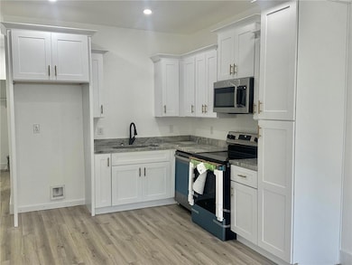 Kitchen with appliances with stainless steel finishes, light wood-type flooring, white cabinetry, dark stone counters, and recessed lighting