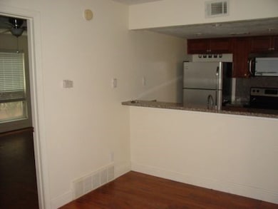 Kitchen with dark wood-style flooring, stainless steel appliances, dark stone countertops, and a peninsula