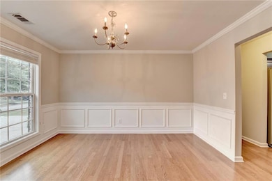 Empty room featuring a chandelier, light wood-type flooring, ornamental molding, and a wainscoted wall
