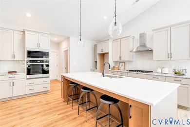 Kitchen with backsplash, a kitchen bar, appliances with stainless steel finishes, decorative light fixtures, and wall chimney exhaust hood