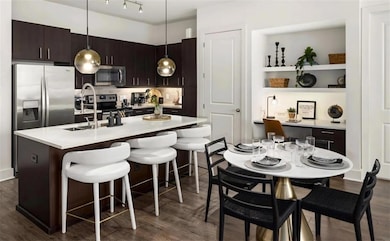 Kitchen featuring an island with sink, dark wood-type flooring, stainless steel appliances, a breakfast bar, and dark brown cabinetry