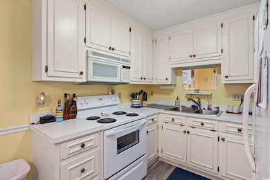 Kitchen with white appliances, a sink, light countertops, white cabinetry, and a textured ceiling