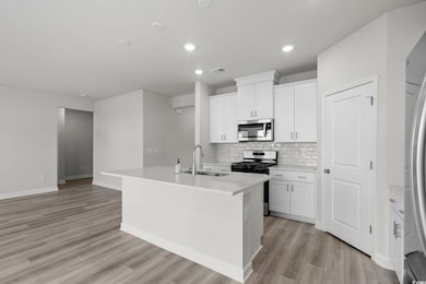 Kitchen featuring a center island with sink, tasteful backsplash, white cabinetry, stainless steel appliances, and light wood-type flooring
