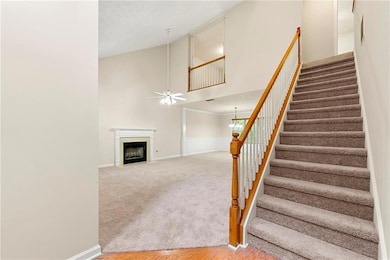Stairs featuring high vaulted ceiling, carpet, a fireplace with flush hearth, a chandelier, and ceiling fan