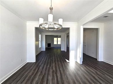 Unfurnished dining area featuring dark wood-style floors, crown molding, a chandelier, and a fireplace with raised hearth