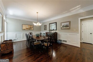 Dining space featuring a chandelier, ornamental molding, dark wood-type flooring, wainscoting, and a decorative wall