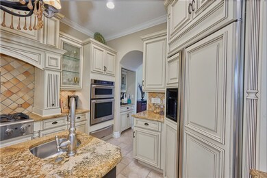 Kitchen featuring cream cabinetry, backsplash, a warming drawer, ornamental molding, and light stone counters